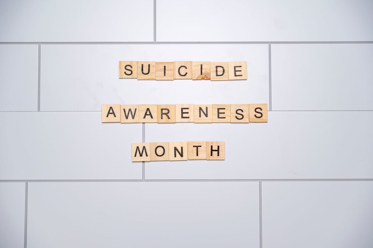 services-04 Wooden tiles spelling 'Suicide Awareness Month' on a white tiled background.